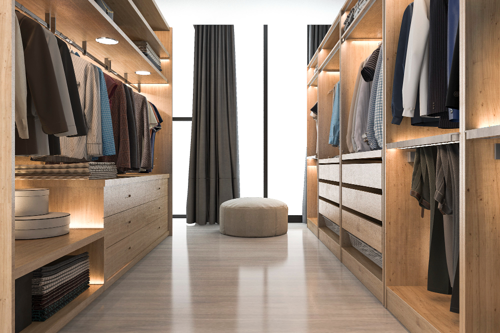 Closet moderno com armários abertos de madeira clara e roupas organizadas, iluminado com luzes embutidas.
