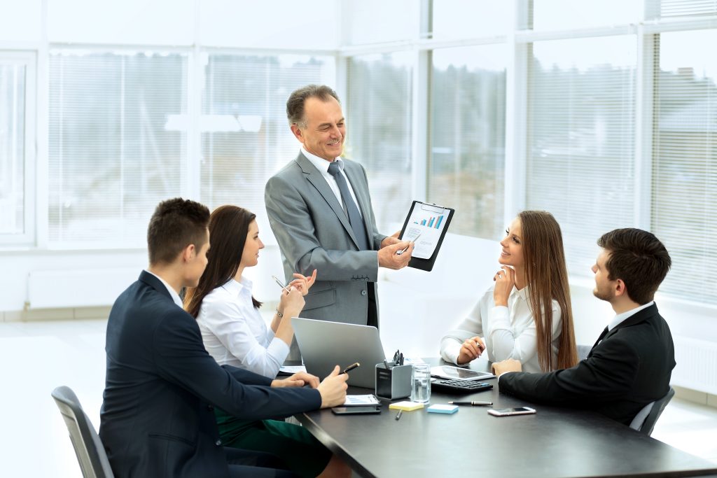 Executivo em reunião com equipe, apresentando gráficos de desempenho em um tablet, em ambiente corporativo moderno.