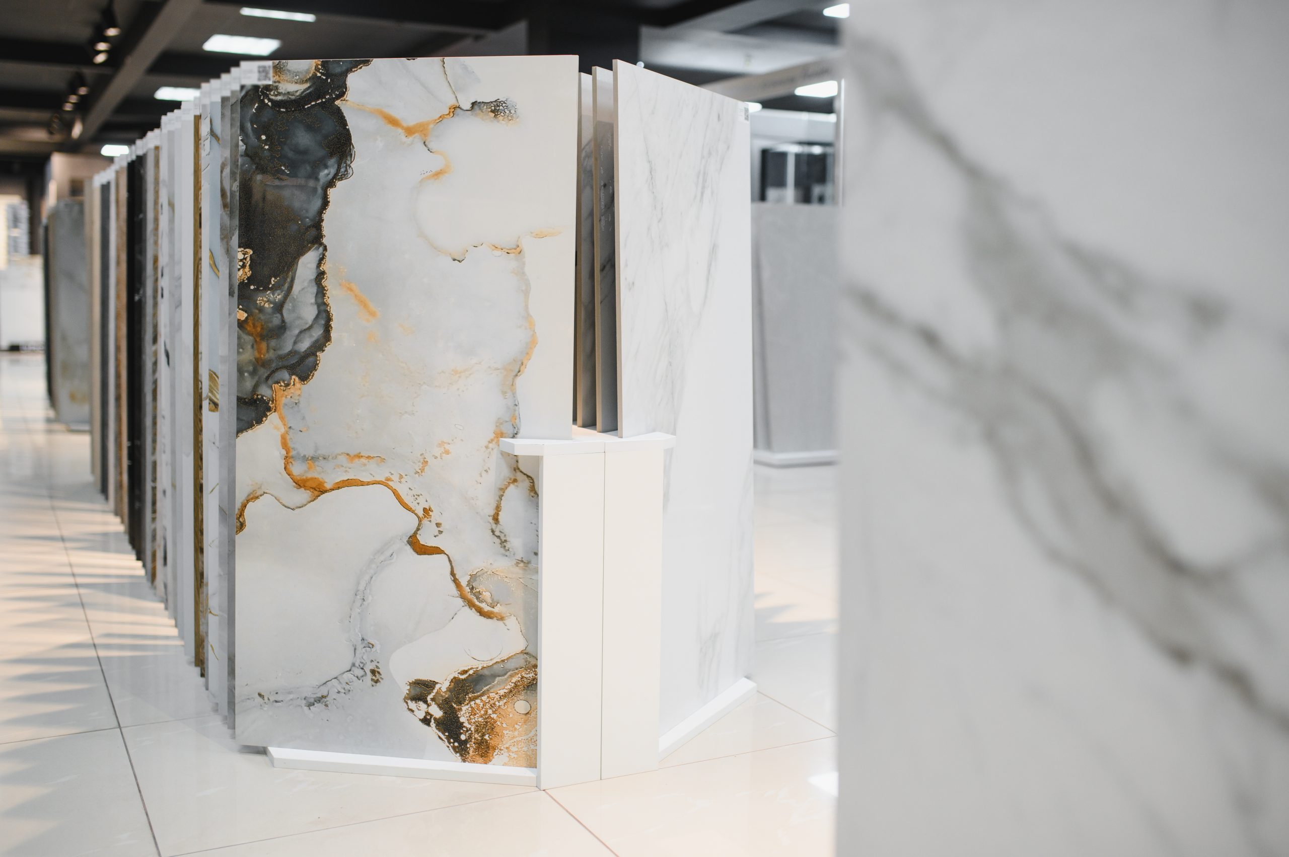 Placas cerâmicas grandes com diferentes acabamentos e padrões expostas em um showroom moderno e bem iluminado.