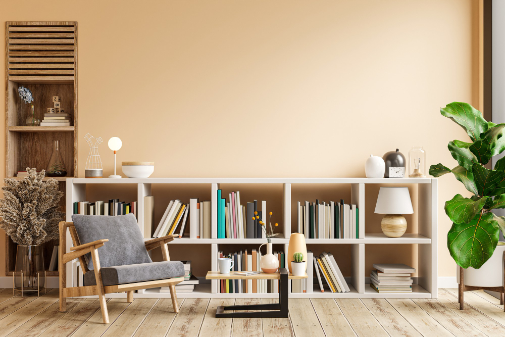 Sala de leitura com poltrona cinza, estante baixa com livros e decoração moderna, em ambiente iluminado e aconchegante.