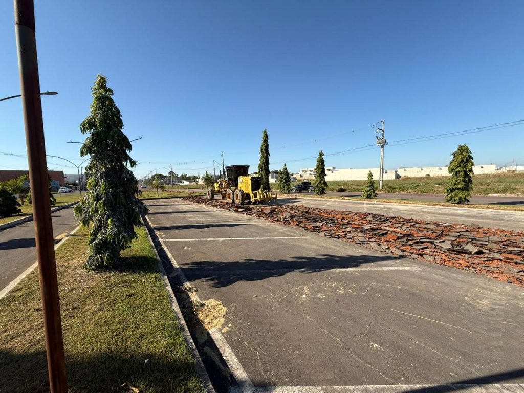Máquina niveladora sobre avenida com asfalto quebrado, em processo de recapeamento.