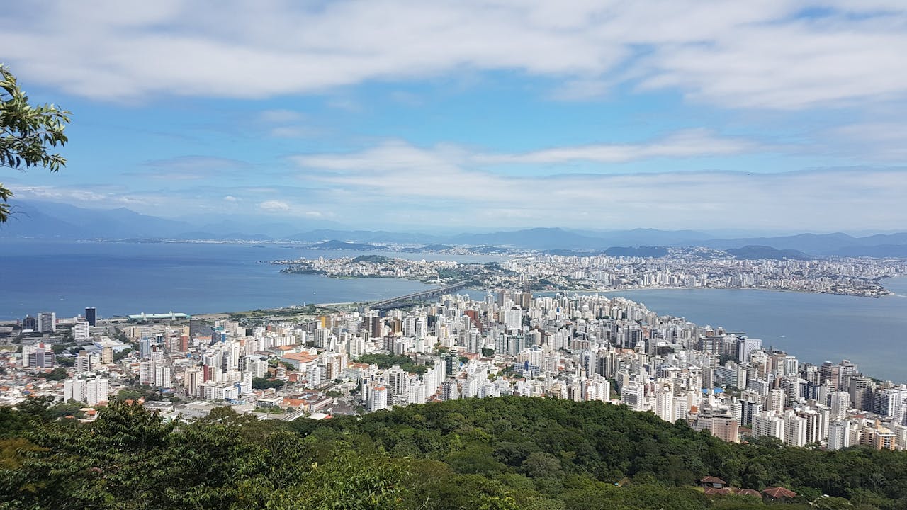 Vista panorâmica de uma cidade litorânea com prédios altos, mar ao fundo e vegetação em primeiro plano.