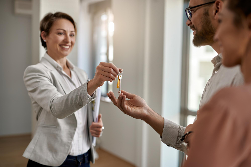 Corretora de imóveis sorridente entrega a chave de um imóvel novo para um casal, simbolizando a compra e a conquista da casa própria.