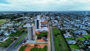 Vista aérea de bairro urbano com prédios residenciais em construção, ruas largas, áreas verdes e casas ao redor.