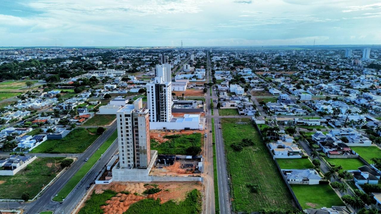 Vista aérea de bairro urbano com prédios residenciais em construção, ruas largas, áreas verdes e casas ao redor.