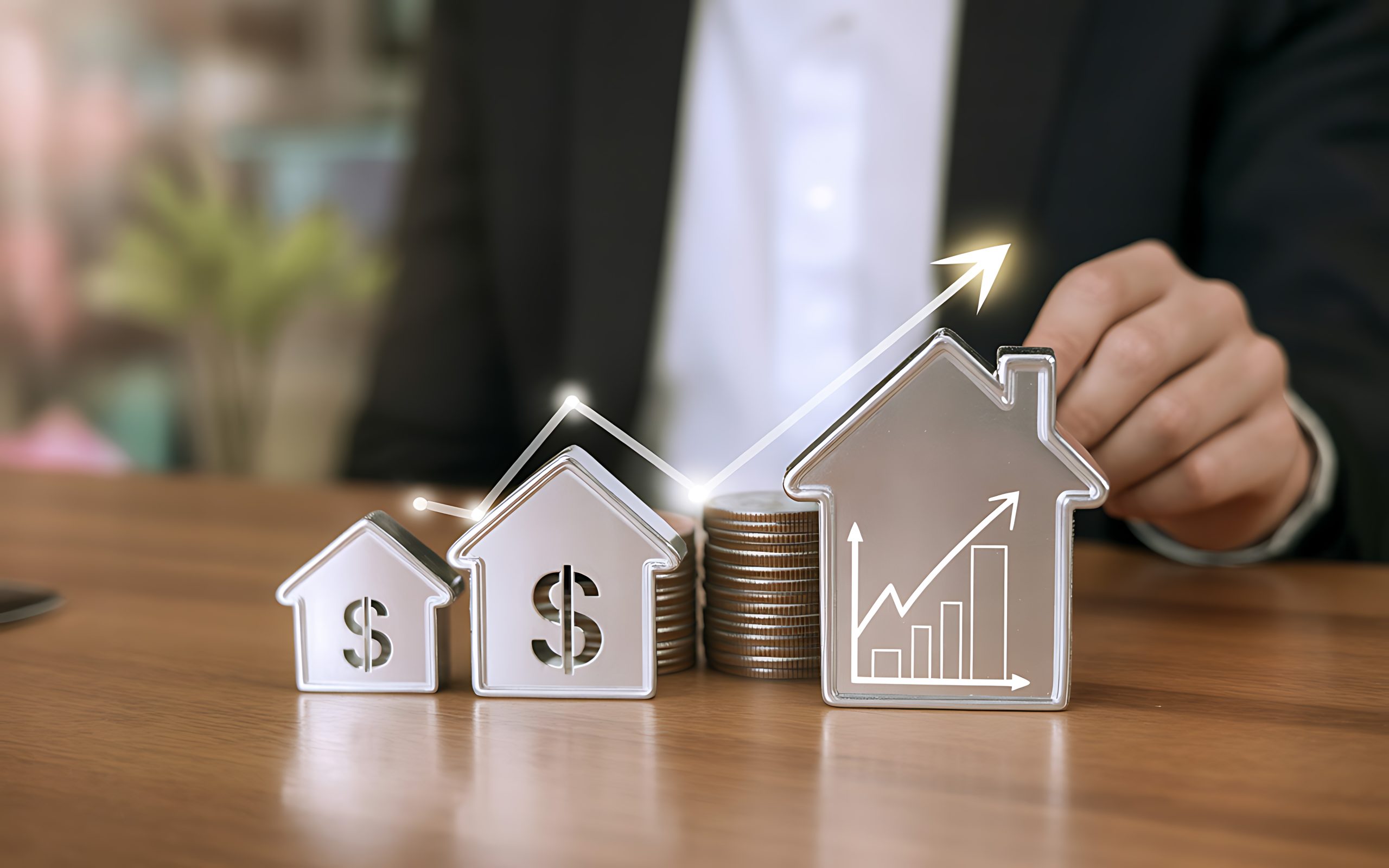 Miniaturas de casas com símbolo de cifrão ao lado de pilhas de moedas e um gráfico em alta, representando a valorização de imóveis e o impacto de índices econômicos como o IGP-M.