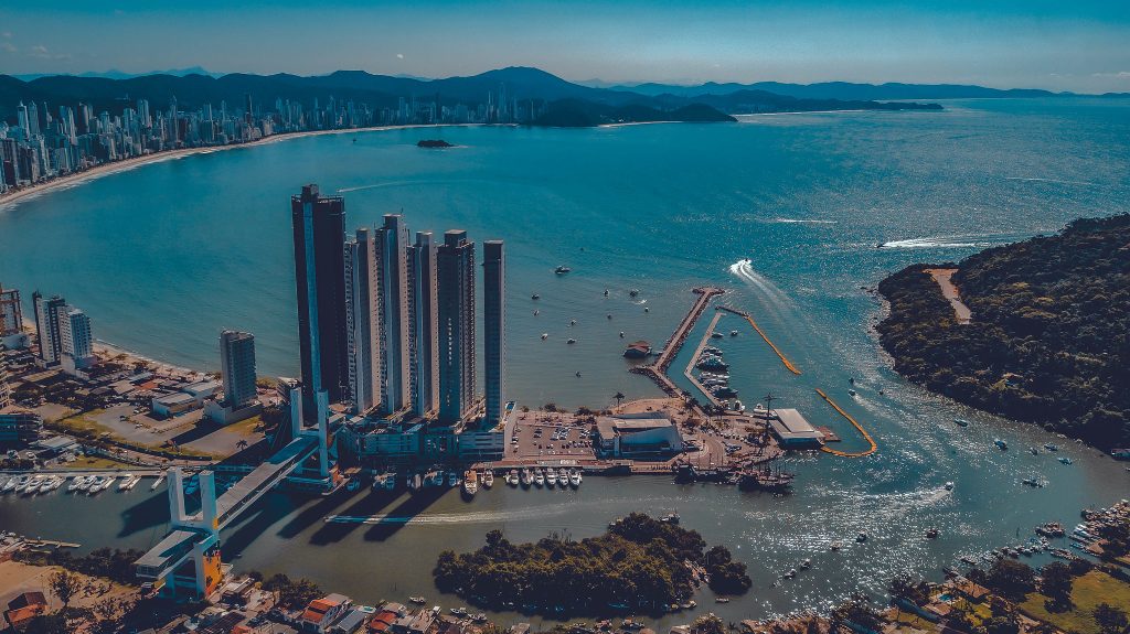 Vista aérea de cidade litorânea com arranha-céus e marina.