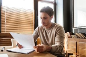 Homem sentado à mesa analisando documentos em um ambiente de escritório iluminado.