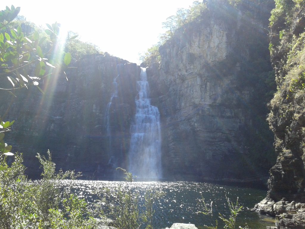 Cachoeira entre rochas com lago e luz do sol.