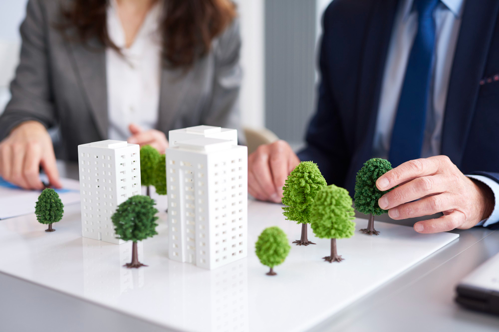 Profissionais analisando maquete urbana com prédios e árvores em reunião de planejamento imobiliário ou urbanístico.